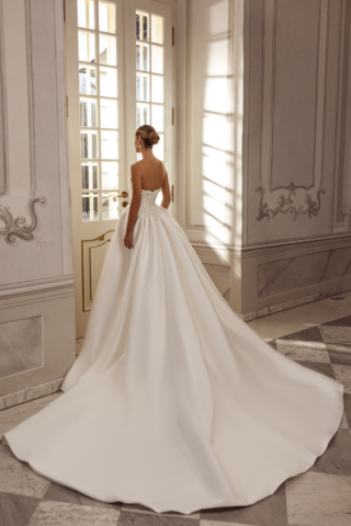 Brautkleid Beatrix von hinten: Die edle Satin-A-Linie beeindruckt mit einem breit fallenden Rock im Prinzessinnen-Stil. Die zarten, glitzernden Blumendetails setzen elegante Akzente an der Taille.
