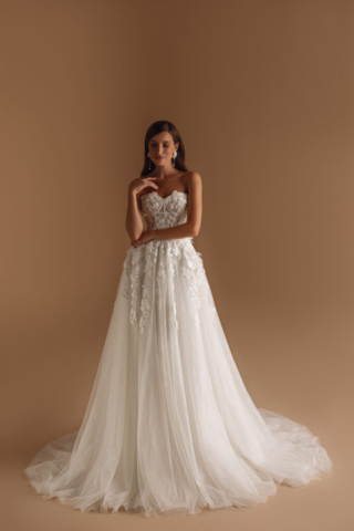 Brautkleid Emryn von vorne: Romantische A-Linie aus Tüll mit einer aufwendig bestickten Korsage. 3D-Blumenapplikationen verleihen dem ärmellosen Design eine verspielte Note, während der leicht fallende Rock mit dezenten Glitzerdetails verzaubert.