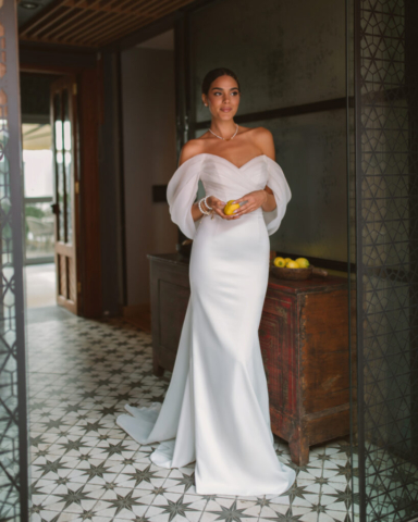 Brautkleid Vetta von vorne: Schlichtes Fit-and-Flare-Design mit einem zarten V-Ausschnitt und fließendem Tüll, der sich sanft um den Oberkörper schmiegt. Die breiten Carmenärmel und die elegante, saubere Silhouette verleihen dem Kleid eine moderne Romantik.