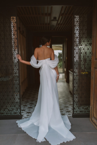 Brautkleid Vetta von hinten: Cleanes Fit-and-Flare-Design mit Carmenärmeln aus softem Tüll und einer langen Schleife, die wie eine Schleppe wirkt. Die besondere Rückansicht sorgt für einen zauberhaften Look.