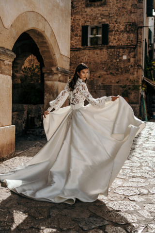 Brautkleid Rhea von hinten: Satinrock mit eleganter Schleppe und tiefen Kellerfalten. Transparentes Spitzenoberteil mit langen, weit ausgestellten Ärmeln und breitem Bund.