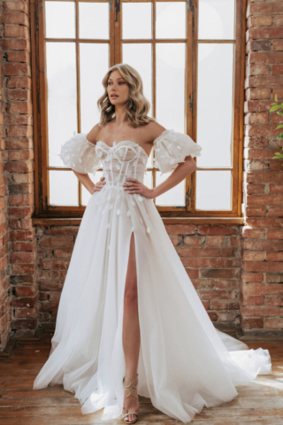 Brautkleid Dreamy: Fließende A-Linie aus Tüll mit hohem Beinschlitz. Die Korsage ist mit transparentem, gerafftem Tüll überzogen und mit 3D-Blätterspritze verziert, die sanft in den Rock übergeht. Abnehmbare Puffärmel sorgen für einen wandelbaren Look