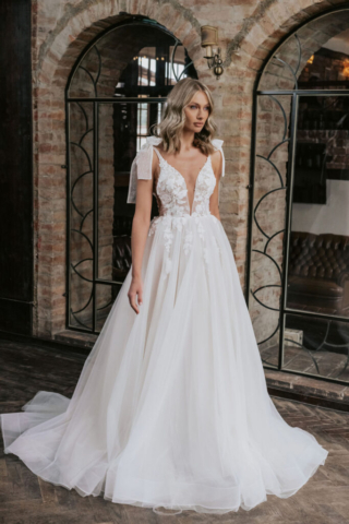 Detail des Brautkleids Ilona: Transparentes Oberteil mit eingearbeiteten Punkten im Tüll. Zarte Schleifen schmücken die Träger an den Schultern, während Blumenapplikationen dem Look eine romantische Note verleihen.